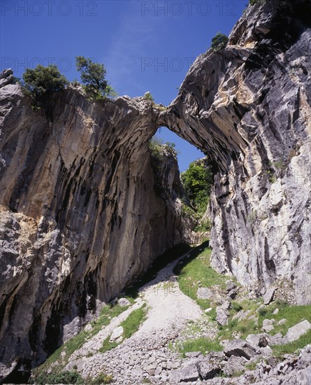 SPAIN, Asturias, Picos de Europa, Garganta del Cares.  Water eroded roofless cave in limestone cliffs framing mountain pathway and view along gorge.