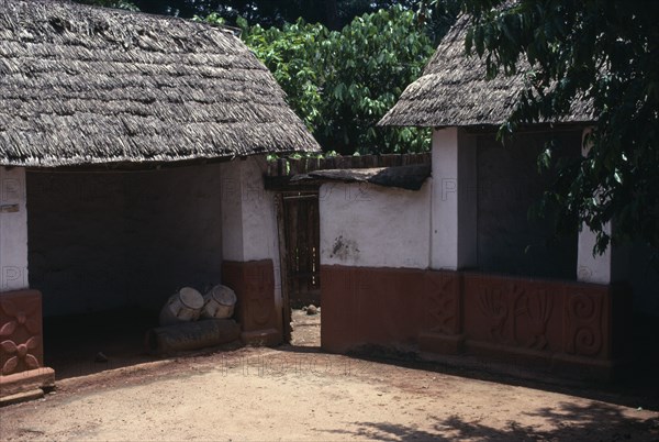 GHANA, Ashanti, Traditional thatched house with intricate patterns on walls. Ceremonial drums inside one of the huts.