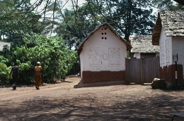 GHANA, Ashanti, Traditional thatched house with intricate patterns on walls. Man and woman walking past.
