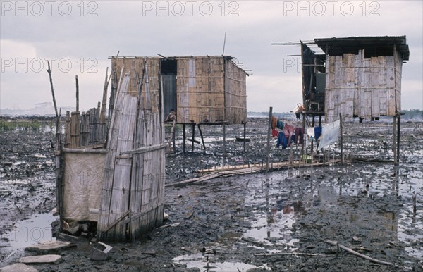 ECUADOR, Guayas Province, Guayaquil , Slum housing with stilt buildings built over untreated sewage. A child seen sitting at doorway and clothes hanging on a washing line above water