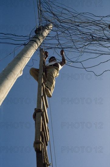 ECUADOR, Guayas Province, Guayaquil , Barrio Indio Guayas slum neighbourhood. Man on ladder illegally connecting into the overhead mains electricity supply.