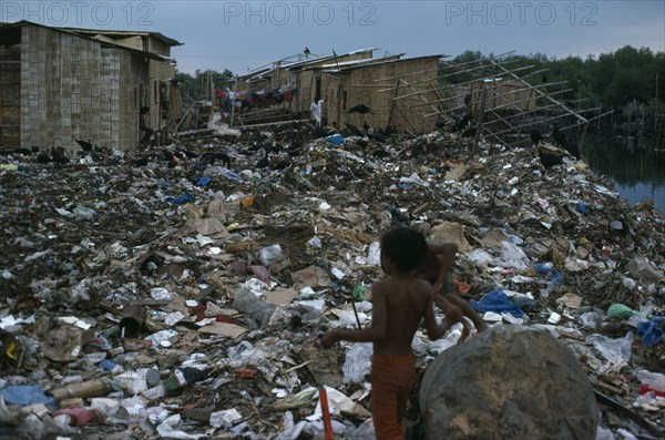ECUADOR, Guayas Province, Guayaquil , The city rubbish tip in barrio Guayas slum neigbourhood with children playing near large rock in the foreground.
