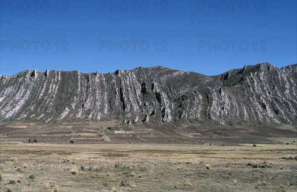BOLIVIA, Altiplano, Vertically folded rock strata behind agricultural land with people and cattle on the ground