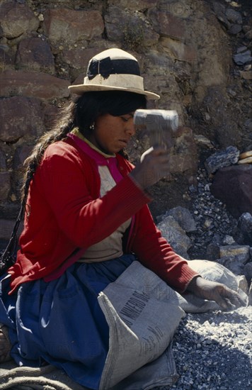 BOLIVIA, Chukiuta, Woman knelling on a Banco Minero de Bolivia sack breaking rocks into small pieces with a hammer at a mine. Near Sucre