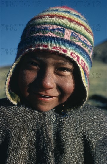 BOLIVIA, , Head and shoulders portrait of a Bolivian boy smiling wearing a colourful wool chullo hat.