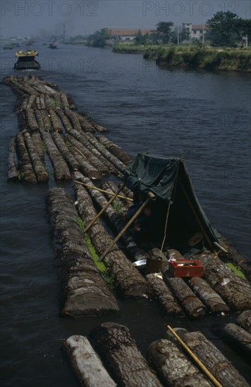 CHINA, Jiangsu Province, Transport, Log rafts on the Grand Canal between Suzhou and Wuxi. Men sheltering under a tent on logs.