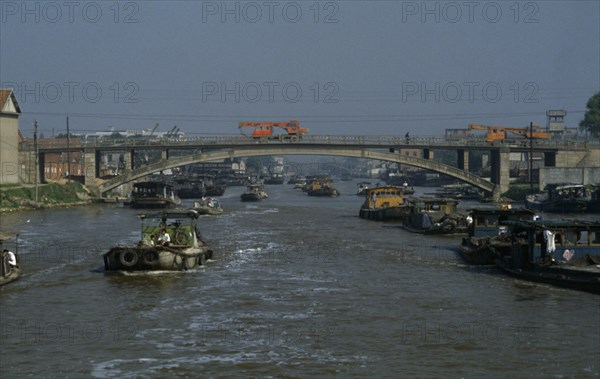 CHINA, Jiangsu Province, Transport, Barges travelling down the Grand Canal between Suzhou and Wuxi. Engineering vehicles driving across bridge over canal.