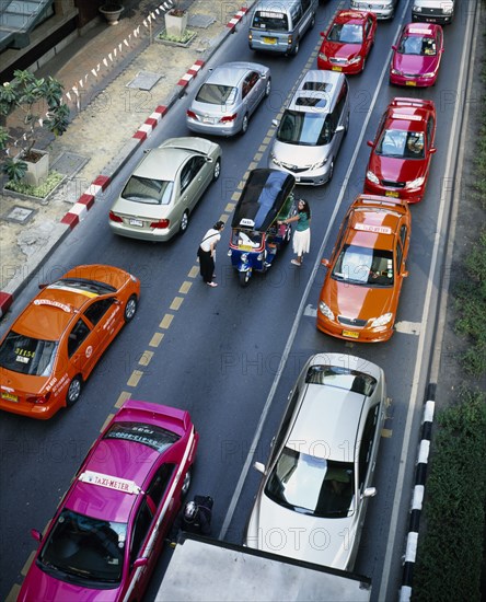 THAILAND, Bangkok, Central, "Thanon Ploenchit opposite Erawan Shrine.  View over three lanes of stationary traffic, brightly coloured meter taxis and two young Western women negotiating with Tuk-tuk driver."