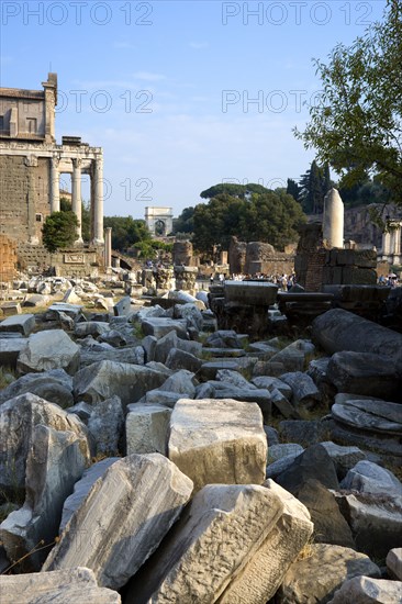 ITALY, Lazio, Rome, Fallen remains of buildings in the Forum with the Temple of Antoninus and Faustina on the left and the Arch of Titus in the distance