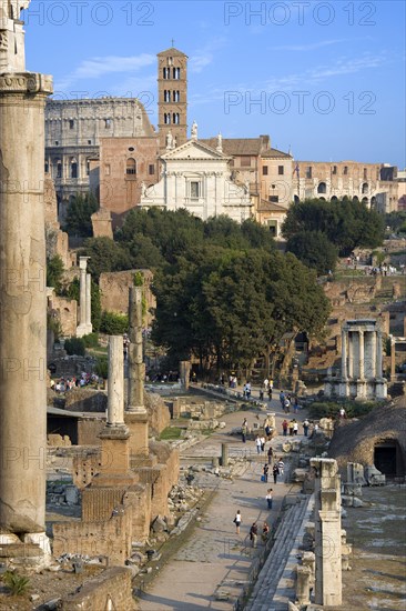 ITALY, Lazio, Rome, View of The Forum with the Colosseum rising behind the bell tower of the church of Santa Francesca Romana with tourists and the Temple of The Vestals in the foreground