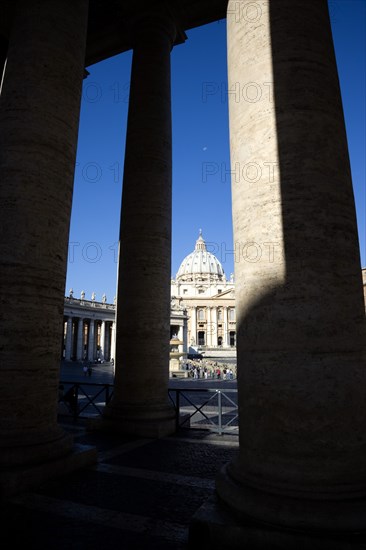 ITALY, Lazio, Rome, Vatican City The Basilica of St Peter and the square or Piazza San Pietro with tourists seen through the columns of Bernini