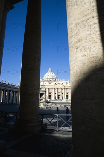 ITALY, Lazio, Rome, Vatican City The Basilica of St Peter and the square or Piazza San Pietro with tourists seen through the columns of Bernini