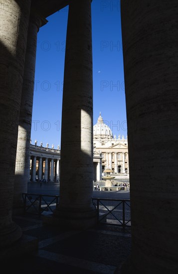 ITALY, Lazio, Rome, Vatican City The Basilica of St Peter and the square or Piazza San Pietro with tourists seen through the columns of Bernini