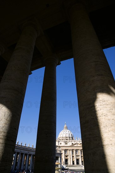 ITALY, Lazio, Rome, Vatican City The Basilica of St Peter and the square or Piazza San Pietro with tourists seen through the columns of Bernini