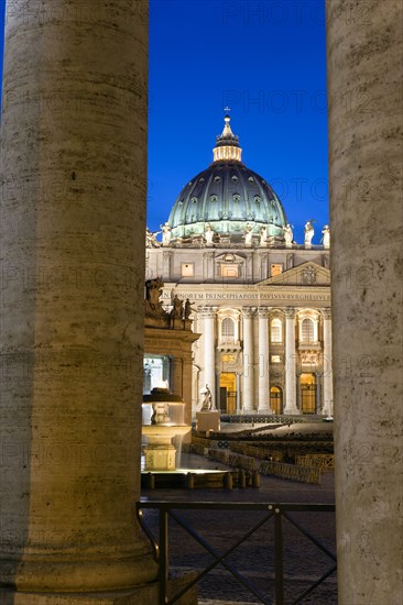 ITALY, Lazio, Rome, Vatican City The Basilica of St Peter and the square or Piazza San Pietro illuminated at night seen through the columns of Bernini