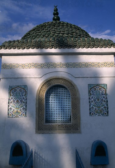 TUNISIA, Nabeul, "Part view of exterior of tomb with domed, tiled roof, arched window and decorative tiles.  Indistinct shadow falling across wall."