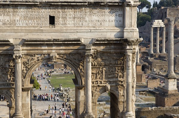 ITALY, Lazio, Rome, The Forum with the triumphal Arch of Septimus Severus in the foreground and the three Corinthian columns of the Temple of Castor and Pollux in the distance with tourists walking around