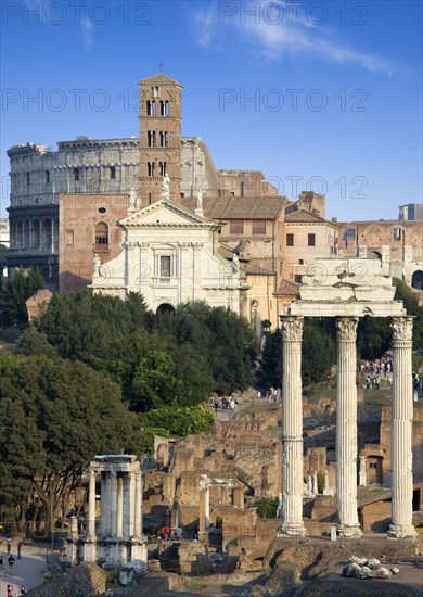 ITALY, Lazio, Rome, View of the Forum with the Colosseum rising behind the bell tower of the church of Santa Francesca Romana with tourists walking past the Temple of Vesta and the three Corinthian columns of the Temple of Castor and Pollux in the foreground