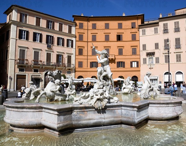 ITALY, Lazio, Rome, The Fountain of Neptune or Fontana del Nettuno in the Piazza Navona with tourists walking past restaurants beyond