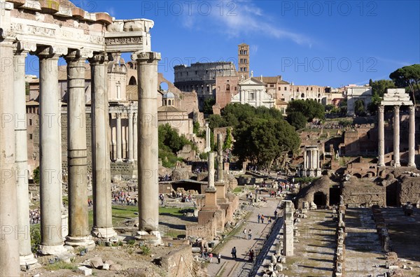 ITALY, Lazio, Rome, The Forum with the Colosseum rising behind the bell tower of Santa Francesca Romana with the columns of The Temple of Saturn on the left and the three Corinthian columns of the Temple of Castor and Pollux on the right with tourists walking around