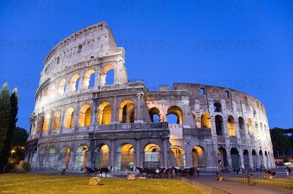 ITALY, Lazio, Rome, The Colosseum illuminated at night with tourists walking around it