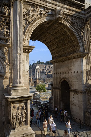 ITALY, Lazio, Rome, Tourists walking through the triumphal Arch of Septimius Severus with the three remaining Corinthian columns of the Temple of Castor and Pollux in the Forum beyond