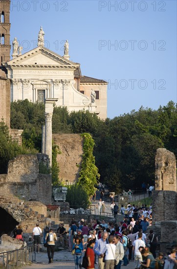 ITALY, Lazio, Rome, Tourists walking past the Temple of Antoninus and Faustina in the Forum with the facade of the church of Santa Francesca Romana beyond