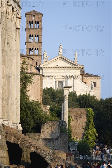 ITALY, Lazio, Rome, Tourists walking past the Temple of Antoninus and Faustina in the Forum with the belltower and facade of the church of Santa Francesca Romana beyond