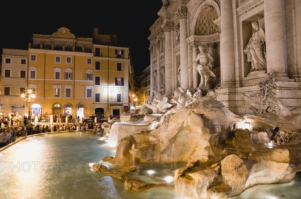 ITALY, Lazio, Rome, The 1762 Trevi Fountain by Nicola Salvi illuminated at night with tourists in the Piazza Di Trevi with tourists in the Piazza di Trevi