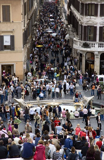 ITALY, Lazio, Rome, The Via dei Condotti the main shopping street busy with people seen from the Spanish Steps with seated tourists and the Fontana della Barcaccia in the foreground