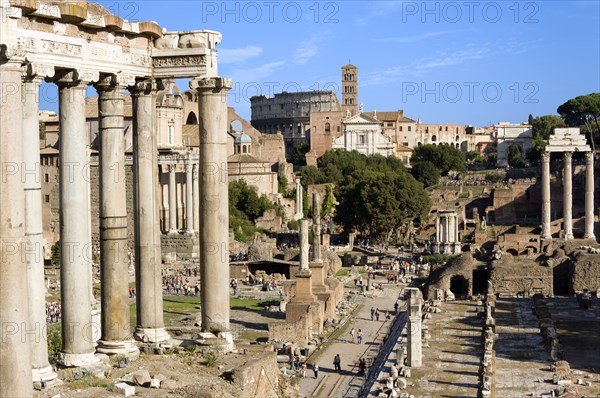 ITALY, Lazio, Rome, "Tourists in the Forum with from left the columns of the Temple of Saturn, the Temple of Antoninus and Faustina, the Temple of Romulus, the Colosseum, the church and belltower of Santa Francesca Romana, the triumphal Arch of Titus, the three Corinthian columns of the Temple of Castor and Pollux with the small Temple of Vesta in the middle "