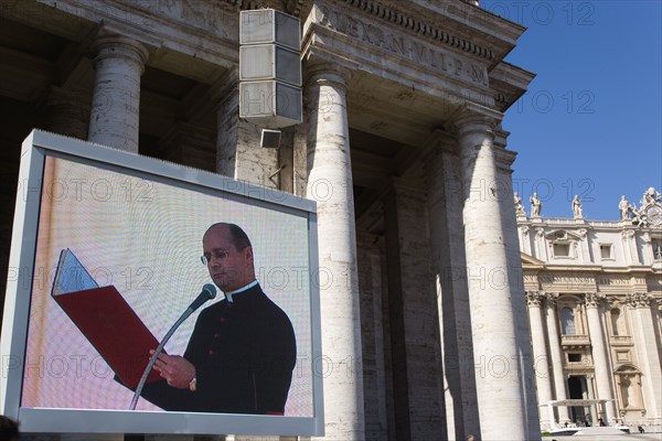 ITALY, Lazio, Rome, Vatican City A cardinal reading from a red book seen on a large video TV monitor display with Pope Benedict XVI Joseph Alois Radzinger seated under a canopy in St Peter's Square for the wednesday Papal Audience in front of the Basilica