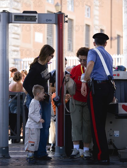 ITALY, Lazio, Rome, Vatican City Women with young boy at x-ray security mchine check manned by a Carabiniere policeman at an entrance to St Peter's Square under the Colonnades for the Wednesday papal audience in the square