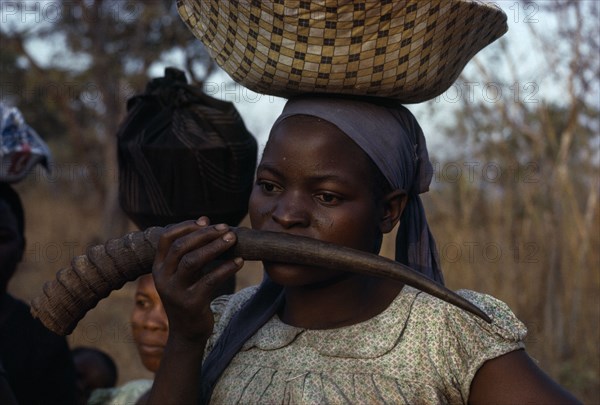 MALAWI, Tribal People, Yau Tribe, Yau woman blowing a water buck horn while carrying a load on her head standing in the fields