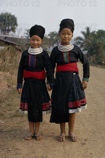 LAOS, Tribal People, Meo Tribe, Full length standing portrait of two Meo girls holding hands and smiling wearing traditional dress and neck rings