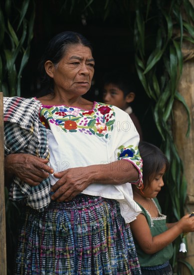 GUATEMALA, Alta Verapaz, Sacaak , Q’eqchi Indian grandmother wearing a traditional embroidered blouse standing with children in a Sacaak refugee settlement