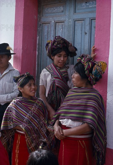 GUATEMALA, El Quiche, Nebaj, Ixil Indian women and girls gathered together at doorway in conversation. Wearing traditional dress with colourful shawls over shoulders and elaborate head-dress wrapped into the hair