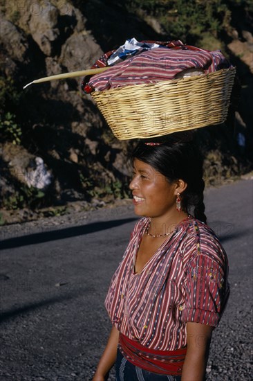 GUATEMALA, Lake Atitlan, Indian girl walking along road carrying a basket of washing on top of her head with a Roman Catholic candle. Near Lake Atitlan