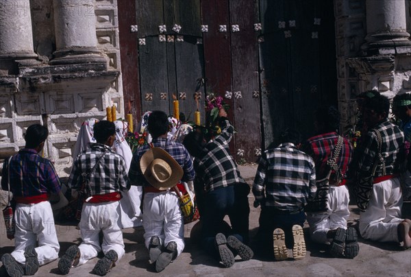GUATEMALA, El Quiche, San Andres de Sajcabaja, Quiche Indian men kneeling in prayer outside the 16th century church during San Andres Festival on December 8th