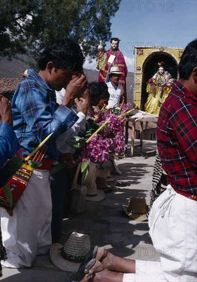 GUATEMALA, El Quiche, San Andres de Sajcabaja, Quiche Indian men knelling in prayer to the saints outside church during San Andres Festival on December 8th