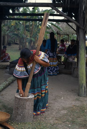 USA, Florida, Everglades, Independent Seminole Native American village. Woman pounding corn wearing traditional colourful patchwork clothing