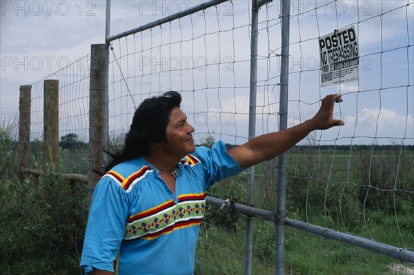 USA, Florida, Everglades, Independent Seminole Native American leader reading a No Trespassing notice posted on fence on agricultural land which is actually Indian land.