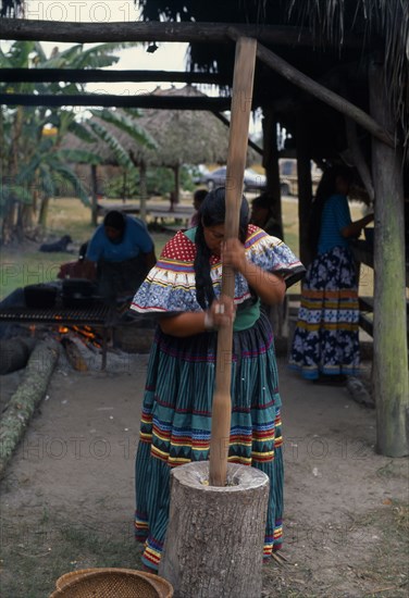USA, Florida, Everglades, Independent Seminole Native American village. Woman pounding corn wearing traditional colourful patchwork clothing