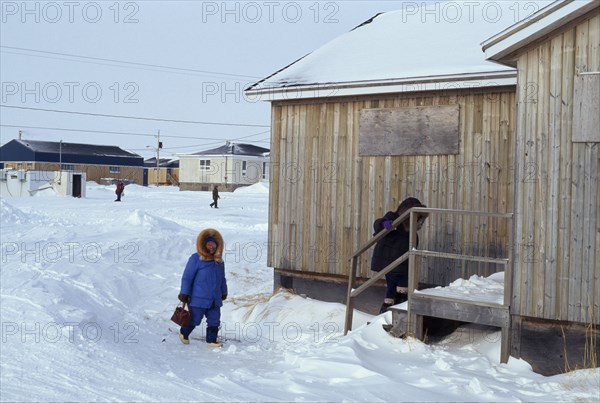 CANADA, Quebec, Hudson Bay, The Great Whale settlement. Cree indigenous community. Women wearing coats with fur hoods walking through deep snow up steps into wood plank family  home. Previously all the community lived in igloos.