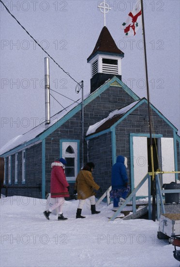 CANADA, Quebec, Hudson Bay, The Great Whale settlement. Cree Indigenous community. Anglican Presbyterian Mission Church with three women walking up the steps through the snow towards main entrance.  Conversion to christianity and the Anglican school system has meant many of the Cree no longer speak their native tongue.