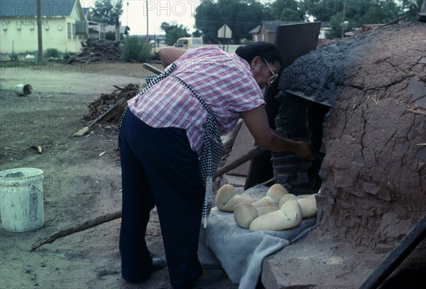 USA, New Mexico, Zuni, Zuni Native American Indian woman making bread in a Horno mud adobe outdoor oven on the Zuni Reservation New Mexico