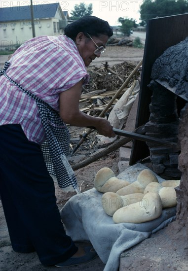 USA, New Mexico, Zuni, "Zuni  Native American Indian woman making bread in a Horno mud adobe outdoor oven in the Zuni Reserve, New Mexico."
