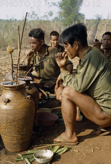 VIETNAM, Central Highlands20092419, Pleimurong village, Vietnam War. Montagnard soldiers relax and drink rice wine through bamboo “straws” from traditional earthenware urns.  20092418