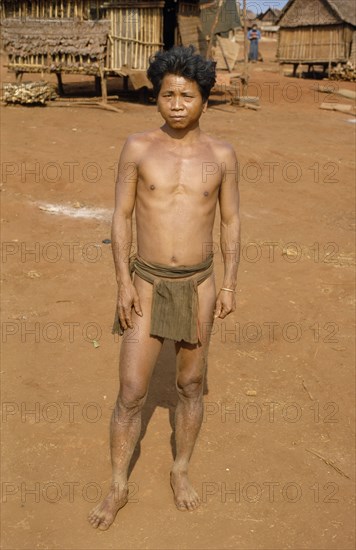 VIETNAM, Central Highlands, Pleimurong village, Vietnam War. Montagnard tribesman in traditional dress in Pleidok refugee camp with typical Montagnard village houses on stilts in background