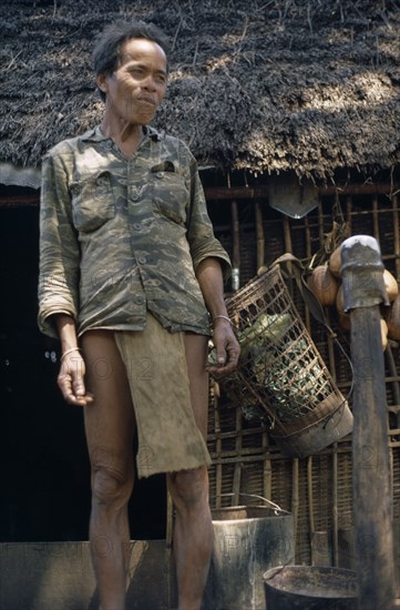 VIETNAM, Central Highlands, Dak Pek, Vietnam War. Montagnard standing next to thatched roof hut at Dak Pek United States and Montagnard Special Forces outpost behind Viet Cong lines in the Central Highlands of South Vietnam
